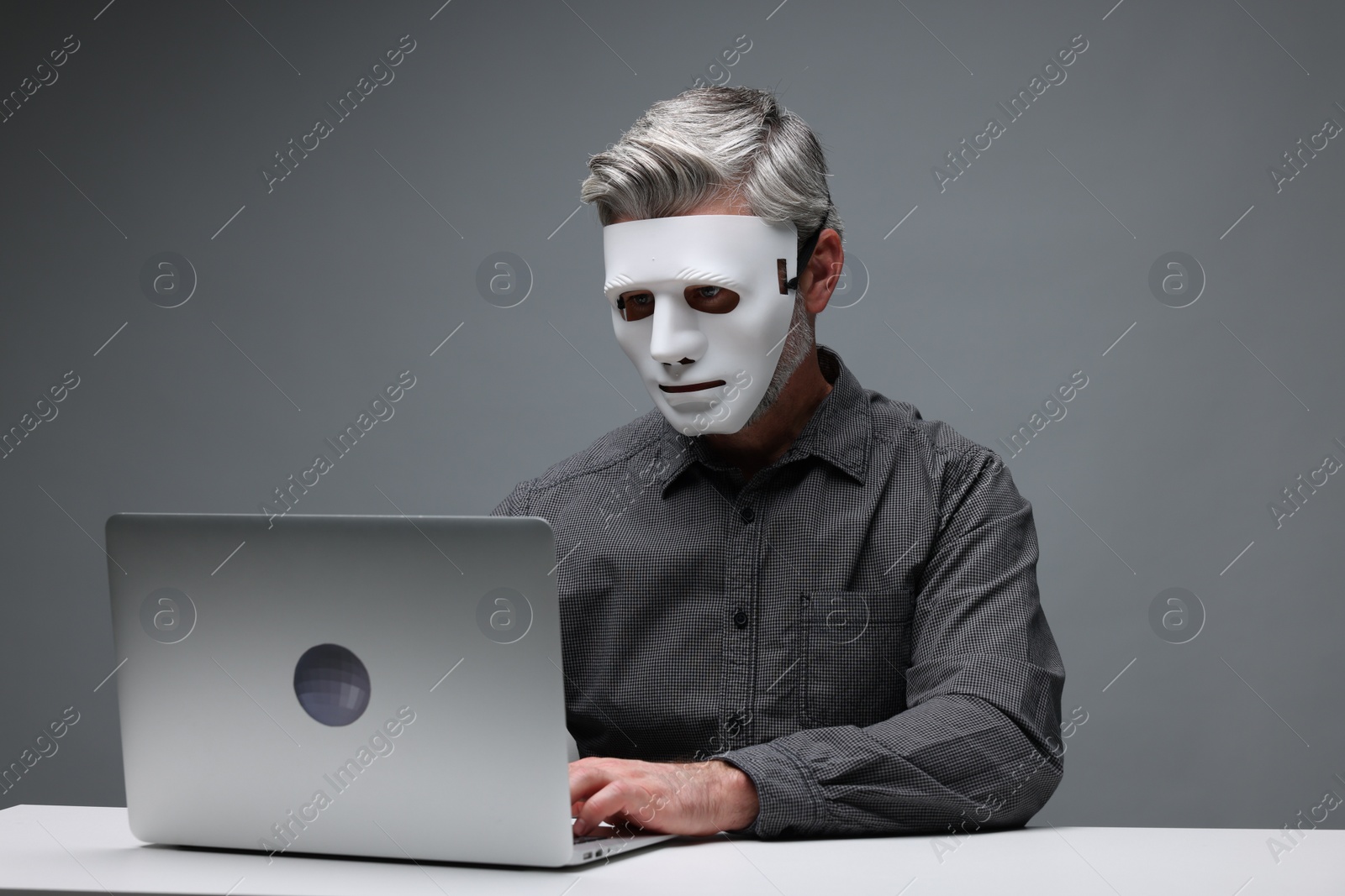 Photo of Man in mask working with laptop at table against grey background