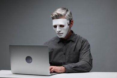 Photo of Man in mask working with laptop at table against grey background