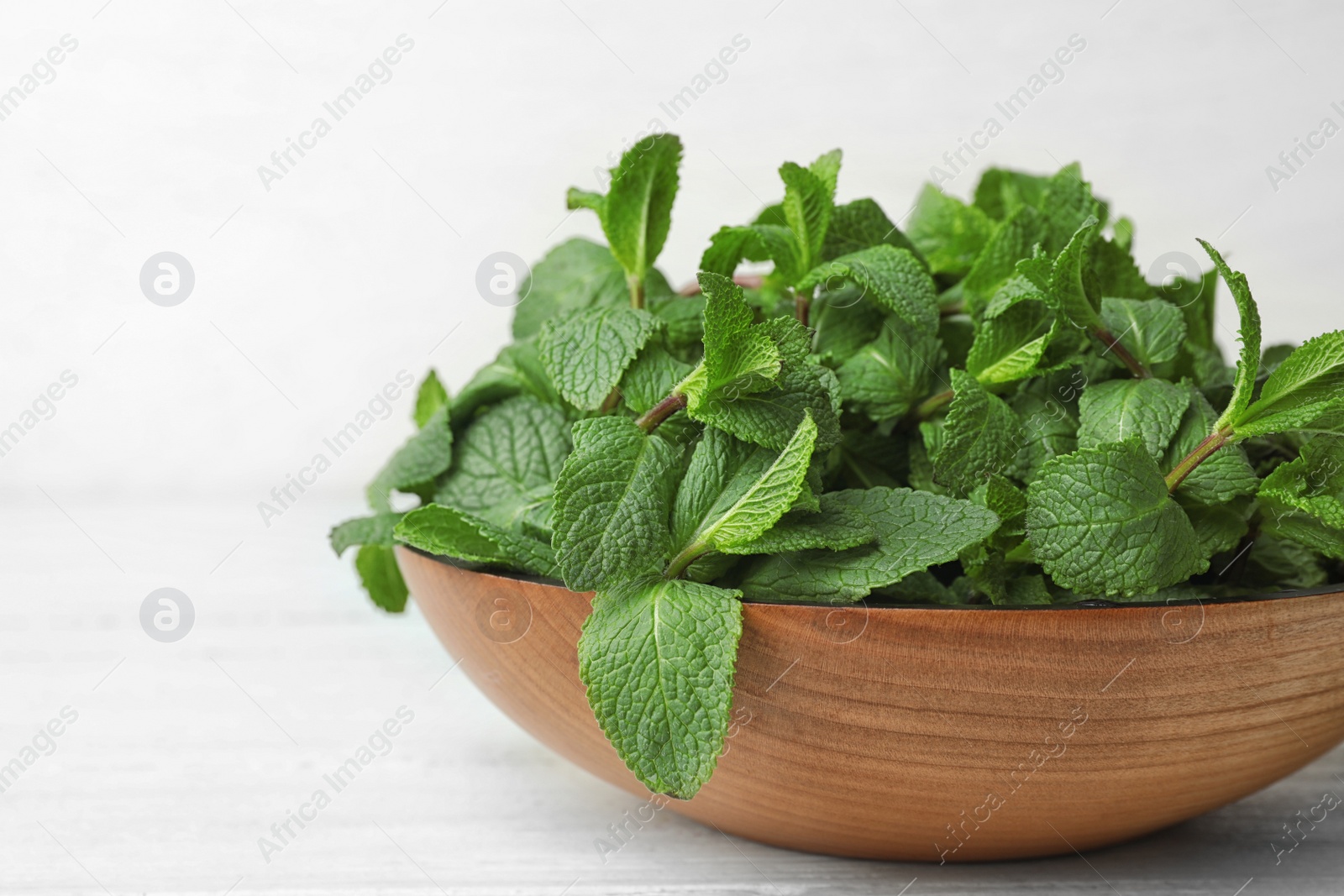 Photo of Wooden bowl with fresh green mint on table, closeup. Space for text