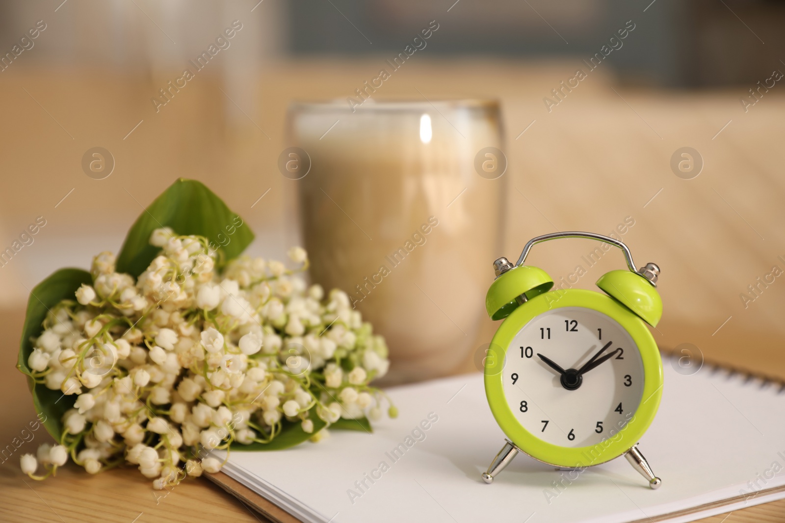 Photo of Cup of aromatic morning coffee, notepad, alarm clock and flowers on wooden table in cafe
