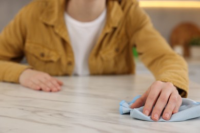 Photo of Woman with microfiber cloth cleaning white marble table in kitchen, closeup