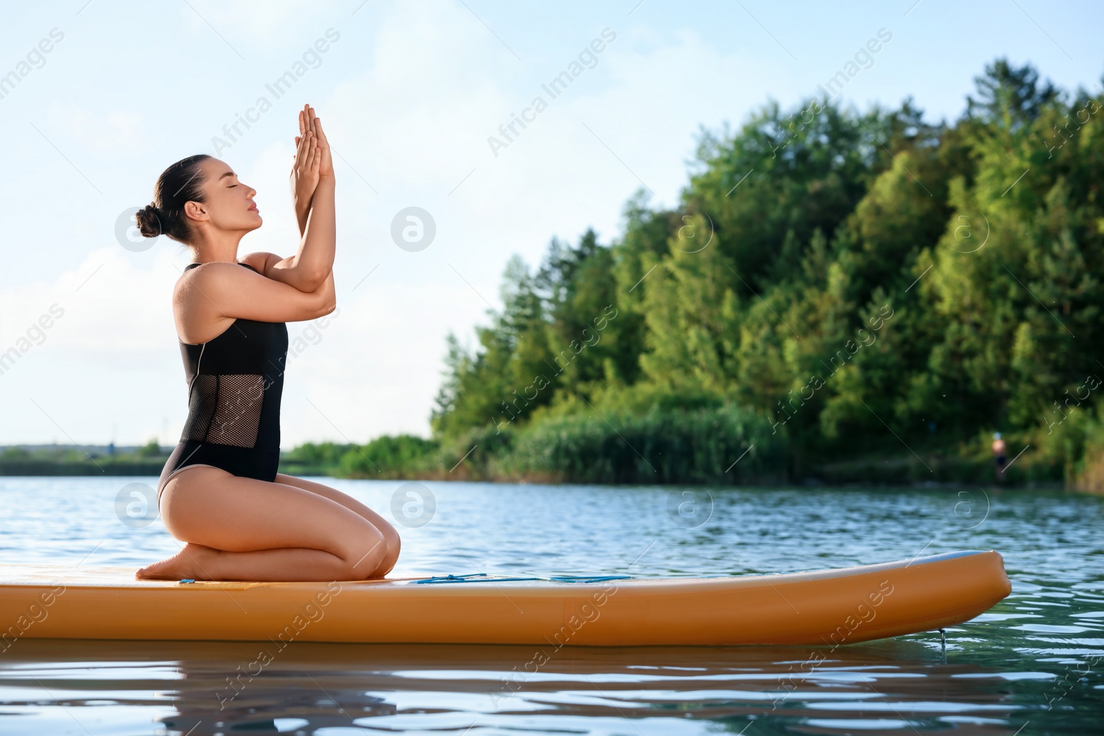 Photo of Young woman practicing yoga on color SUP board on river