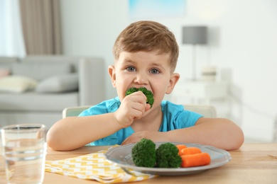 Photo of Adorable little boy eating vegetables at table in room