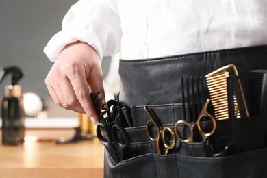 Photo of Hairstylist with professional tools in waist pouch in salon, closeup
