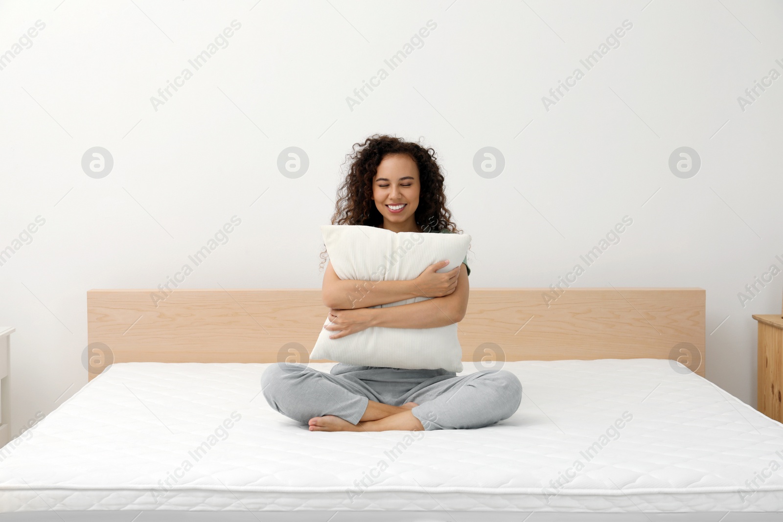 Photo of Happy young African American woman hugging pillow on bed with comfortable mattress at home