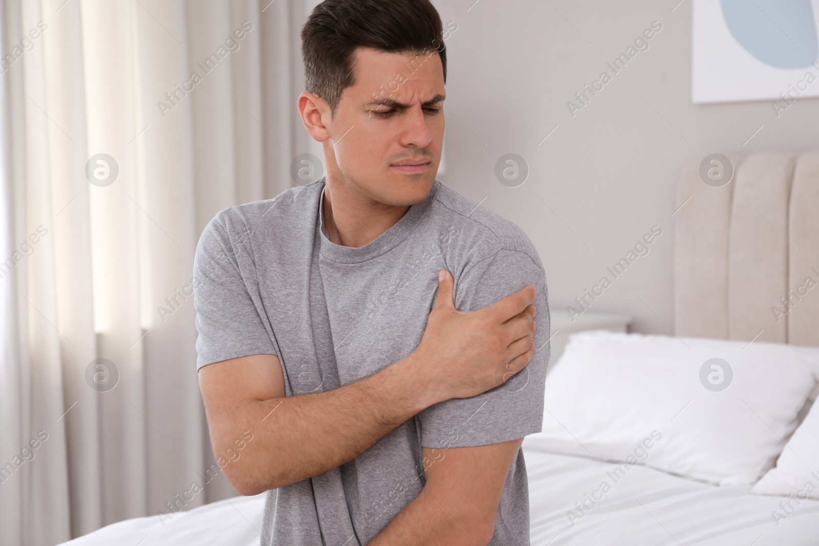 Photo of Man suffering from shoulder pain on bed at home