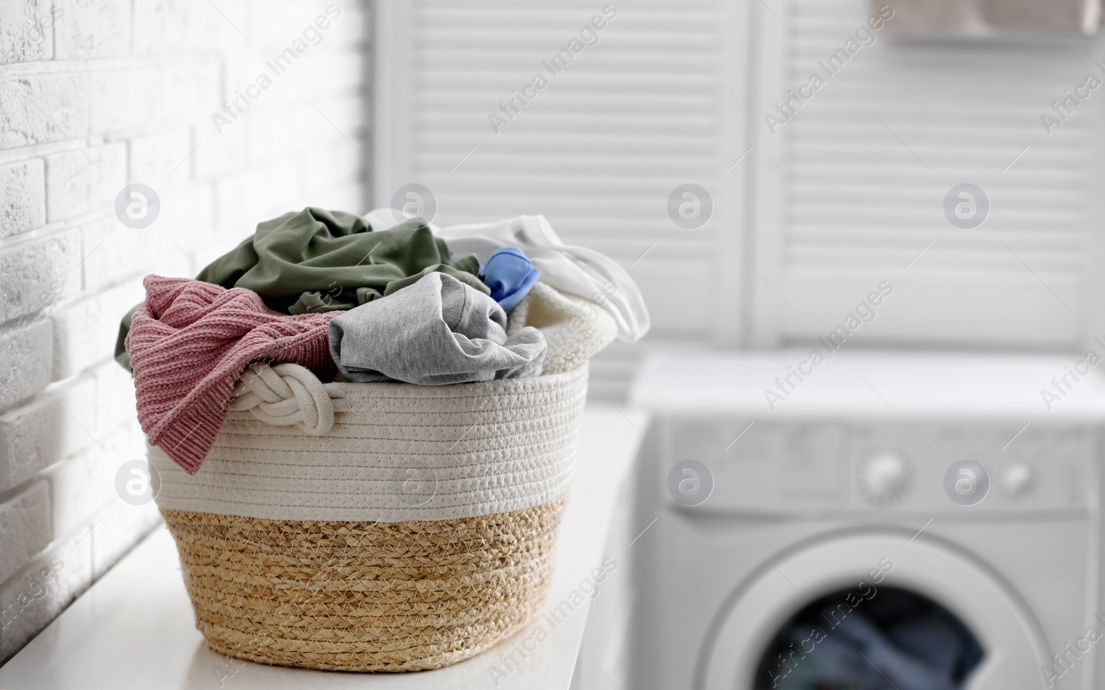 Photo of Wicker basket with dirty laundry indoors, space for text