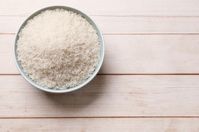 Photo of Raw basmati rice in bowl on white wooden table, top view. Space for text