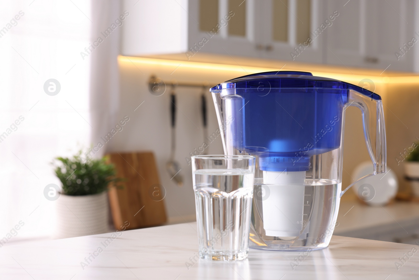 Photo of Water filter jug and glass on white marble table in kitchen, closeup. Space for text