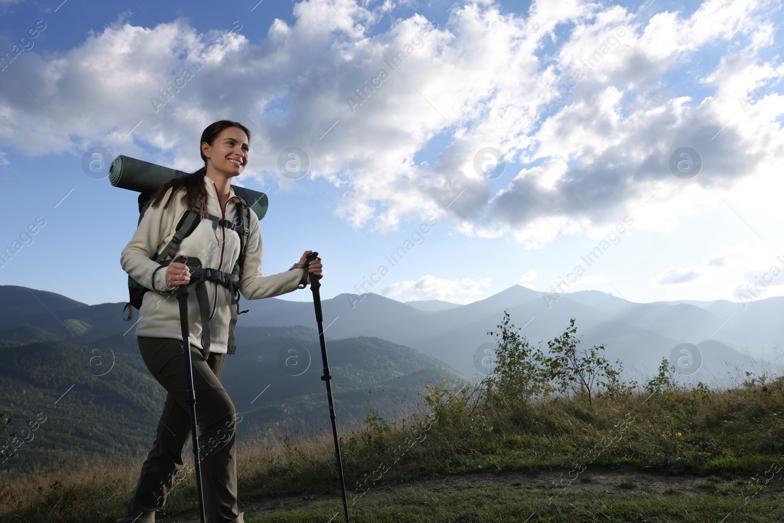 Photo of Tourist with backpack and trekking poles hiking through mountains, space for text