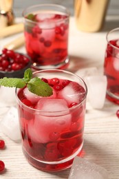 Photo of Tasty cranberry cocktail with ice cubes and mint in glasses on table, closeup