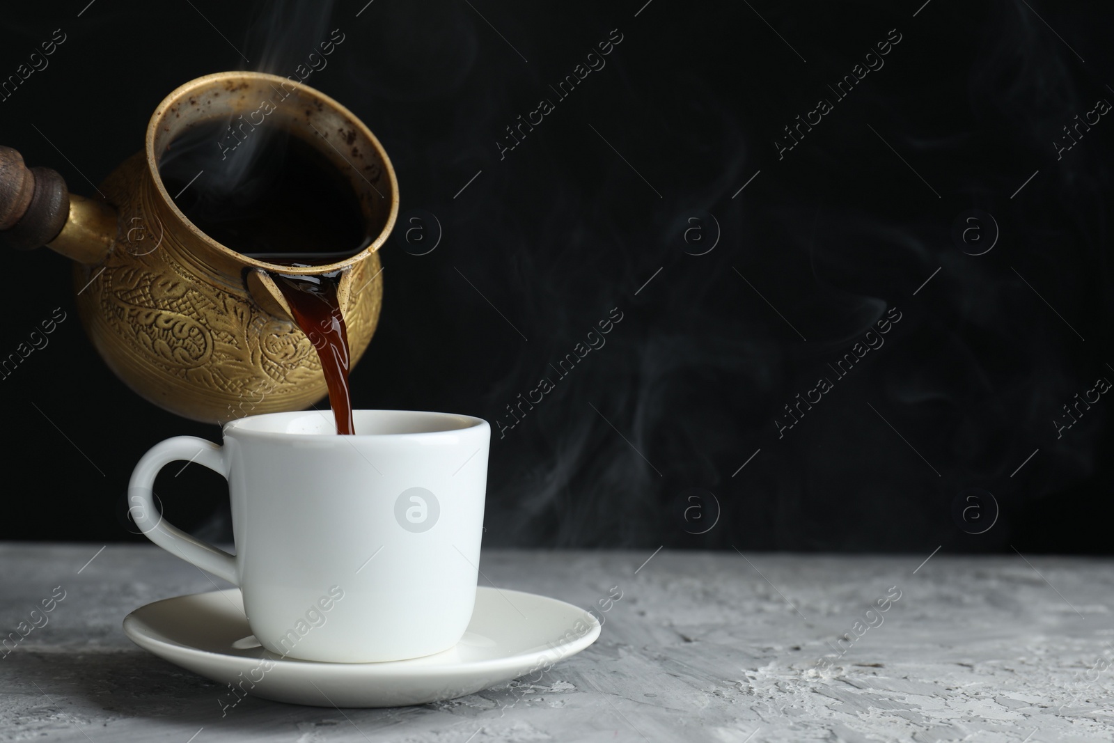 Photo of Turkish coffee. Pouring brewed beverage from cezve into cup at grey table. Space for text