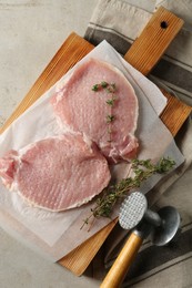 Photo of Cooking schnitzel. Raw pork chops, thyme and meat mallet on grey table, top view