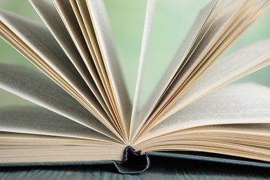 Photo of Open book on blue wooden table against blurred green background, closeup
