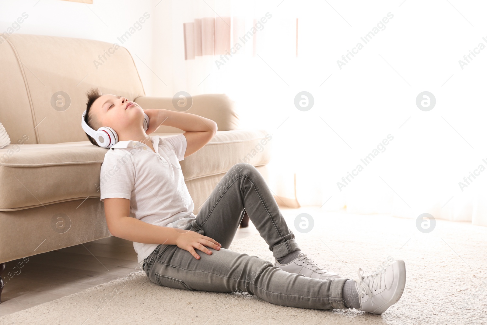 Photo of Little boy listening to music near sofa at home