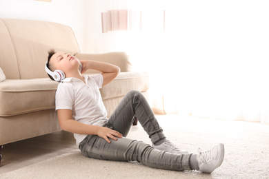 Photo of Little boy listening to music near sofa at home