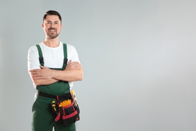 Photo of Portrait of professional construction worker with tool belt on grey background, space for text