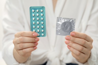 Photo of Woman holding condom and contraceptive pills, closeup. Choosing birth control method