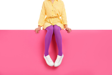 Woman wearing bright tights and stylish shoes sitting on color background, closeup