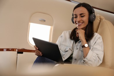 Photo of Young woman with tablet and headphones listening to music in airplane during flight