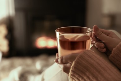 Photo of Woman with cup of tea resting near fireplace at home, closeup