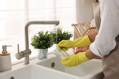 Woman washing glass at sink in kitchen, closeup