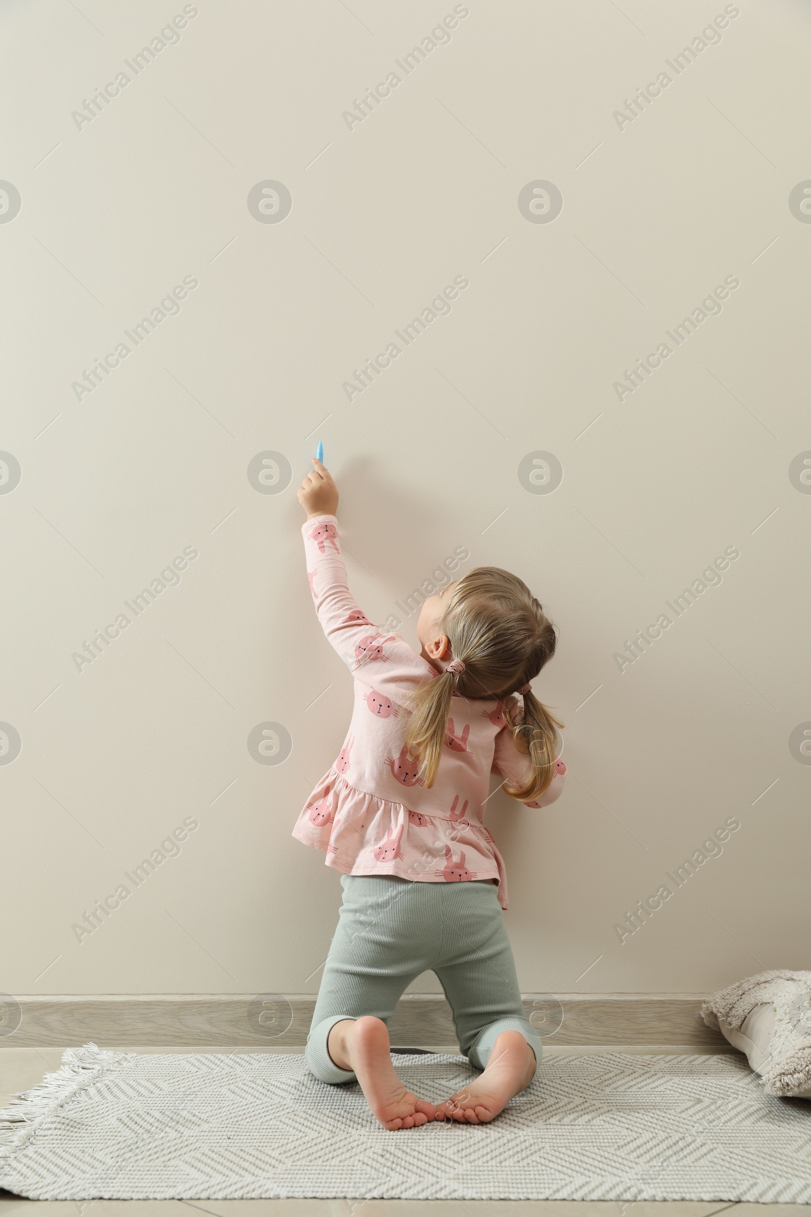 Photo of Little girl drawing on beige wall indoors, back view. Child`s art