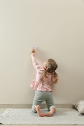 Little girl drawing on beige wall indoors, back view. Child`s art