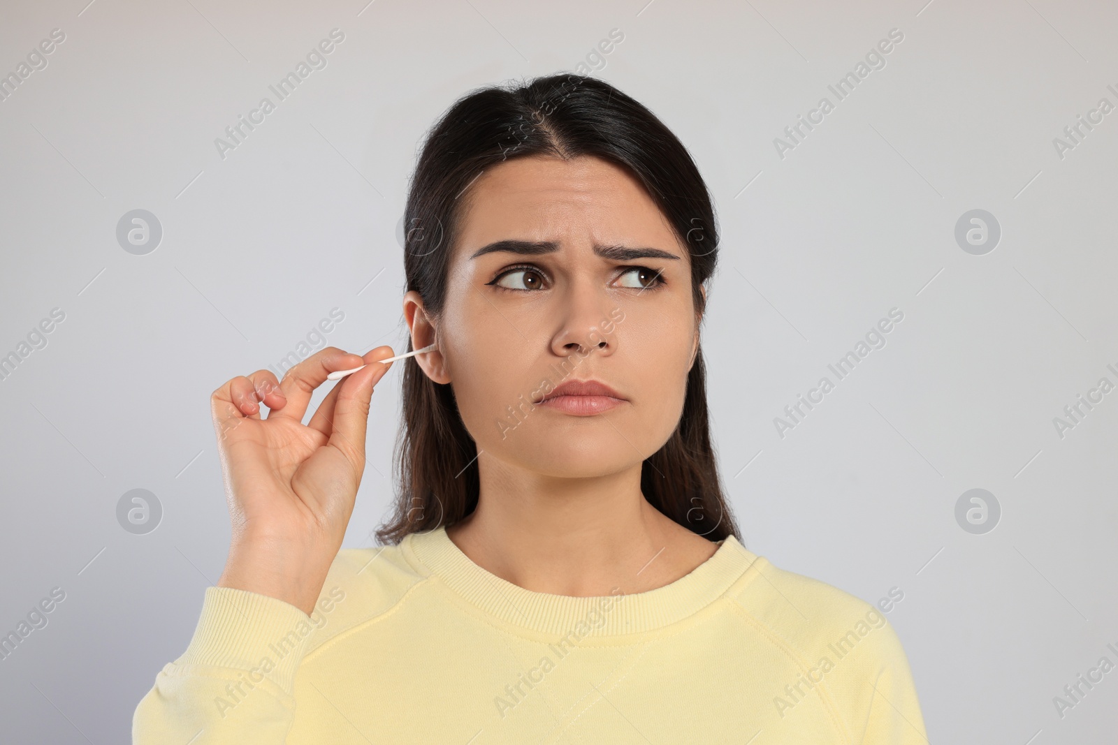 Photo of Young woman cleaning ear with cotton swab on light grey background