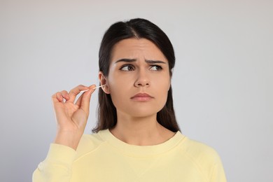 Photo of Young woman cleaning ear with cotton swab on light grey background