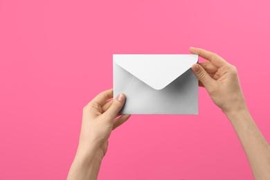 Photo of Woman holding white paper envelope on pink background, closeup