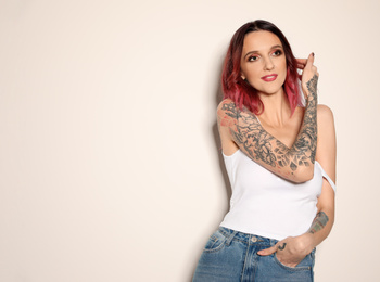 Beautiful woman with tattoos on arms against light background. Space for text