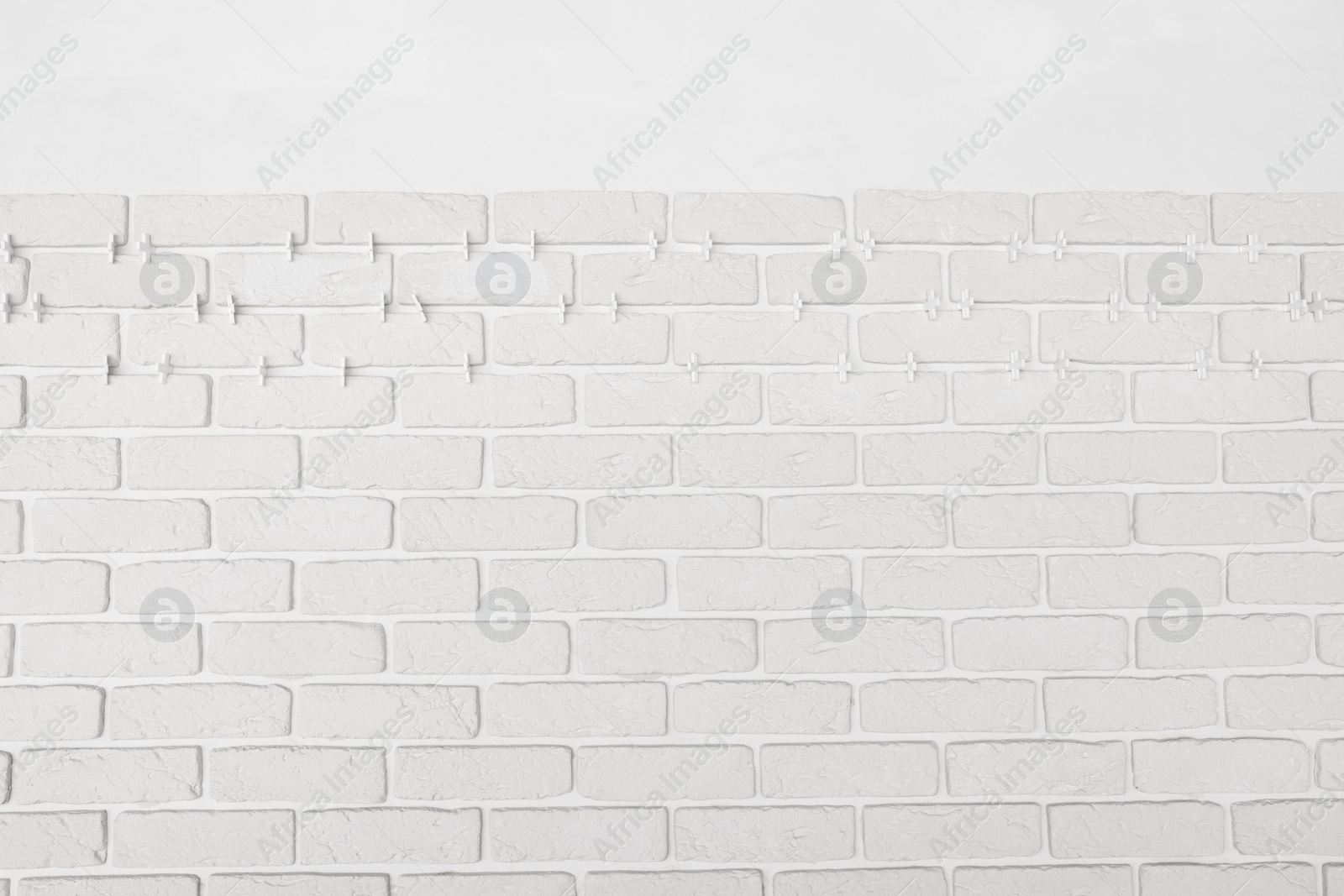 Photo of Decorative white bricks with tile leveling system on wall