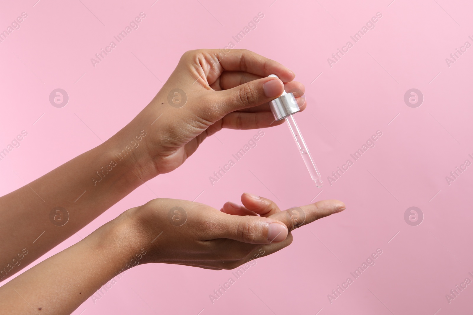 Photo of Woman applying cosmetic serum onto her finger on pink background, closeup