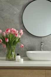 Vase with beautiful pink tulips near sink in bathroom