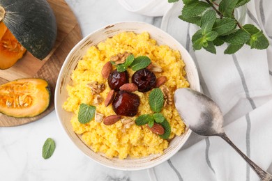 Photo of Tasty cornmeal with dates, nuts and mint in bowl served on white marble table, flat lay