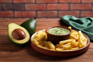 Photo of Plate with french fries, guacamole dip and avocado served on wooden table