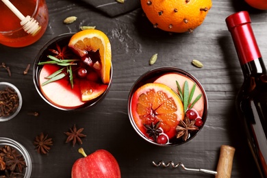 Photo of Cups of tasty mulled wine on black wooden table, flat lay