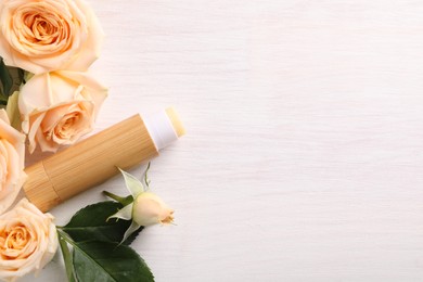 Lip balm and rose flowers on white wooden background, flat lay. Space for text