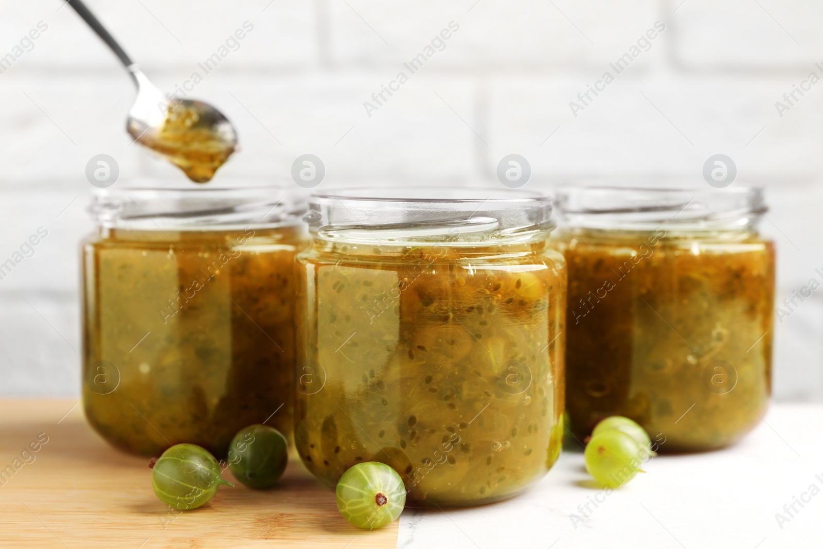 Photo of Jars of delicious gooseberry jam and fresh berries on white table, closeup