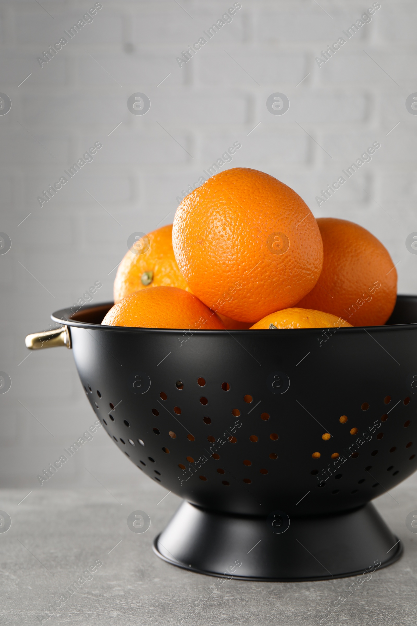 Photo of Fresh ripe oranges in black colander on light grey table