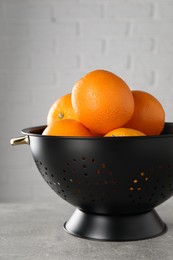 Photo of Fresh ripe oranges in black colander on light grey table