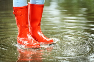 Photo of Woman with red rubber boots in puddle, closeup. Rainy weather