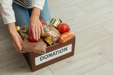 Photo of Woman taking food from donation box on wooden floor, closeup with space for text