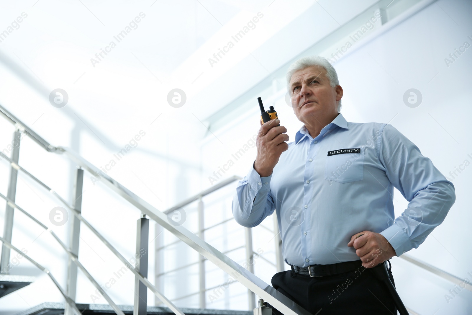 Photo of Professional security guard with portable radio set on stairs indoors
