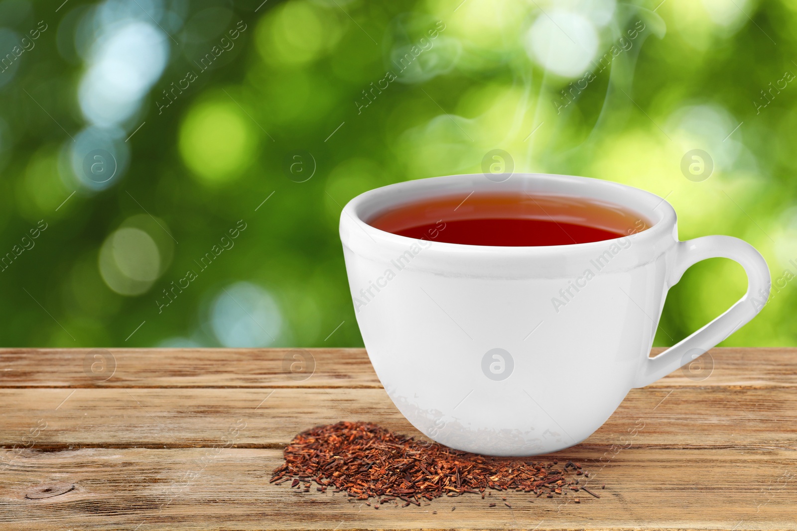 Image of Cup of hot freshly brewed rooibos tea on wooden table outdoors