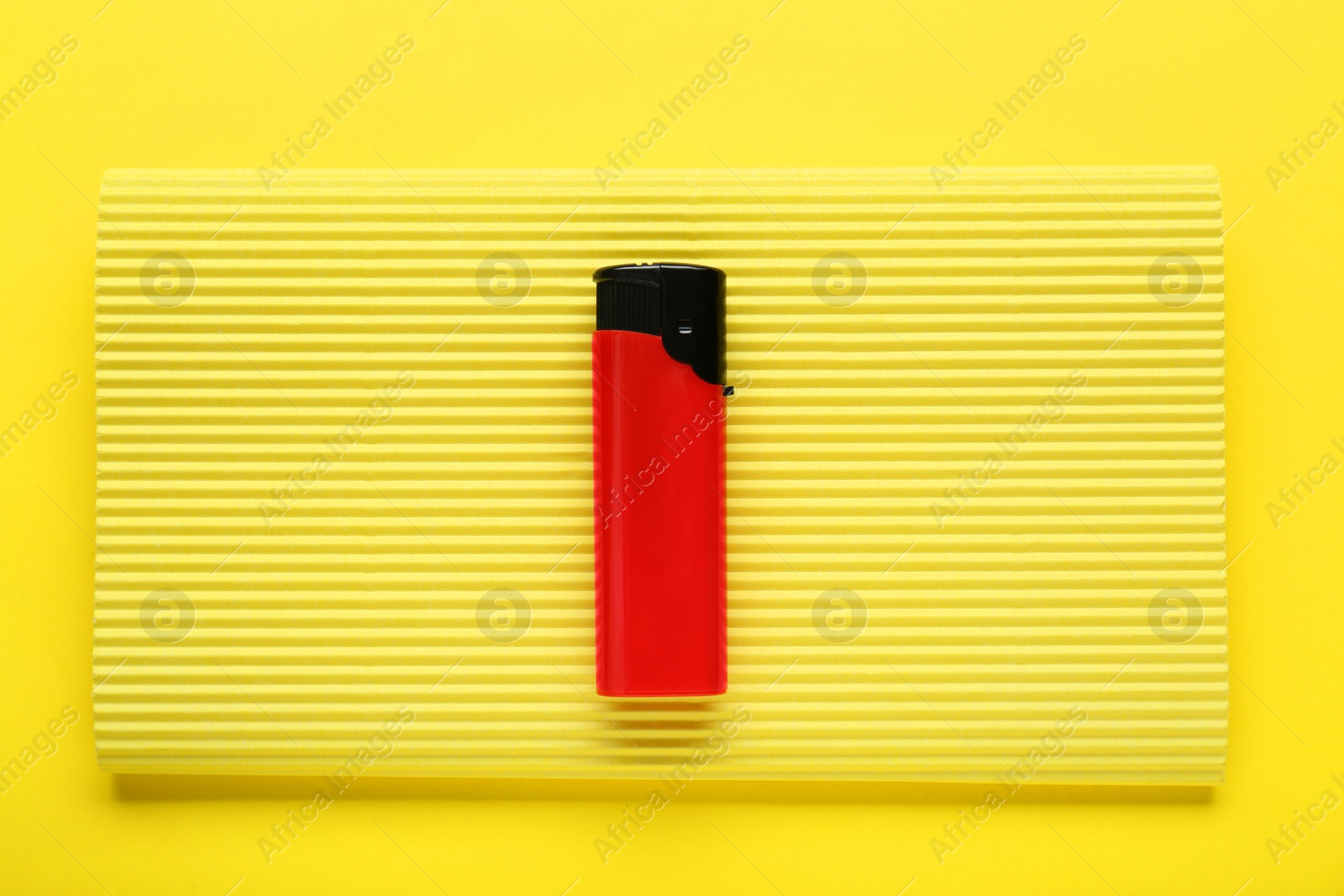 Photo of Stylish small pocket lighter with corrugated fiberboard on yellow background, top view