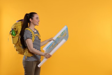 Photo of Smiling young woman with backpack and map on orange background, space for text. Active tourism