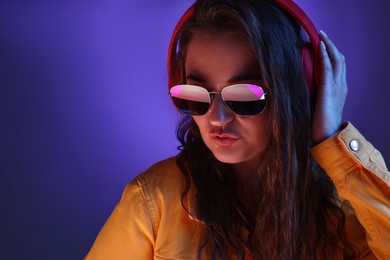 Portrait of beautiful young woman with headphones on color background with neon lights