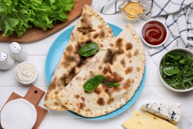 Photo of Delicious cheese calzones and products on white wooden table, flat lay